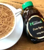 a 450g jar of date syrup next to a cup of cappuccino