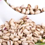 A mass or pile of jumbo pistachio next to a bowl