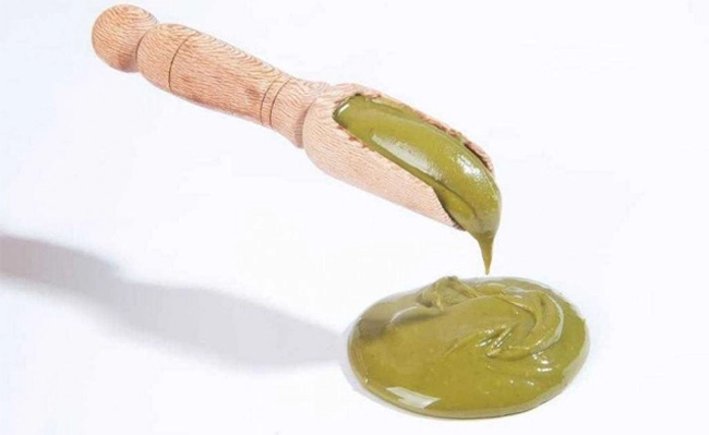 Green pistachio paste dripping from a dipper.